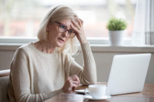 Uma mulher idosa colocou a mão na testa enquanto olha para o computador