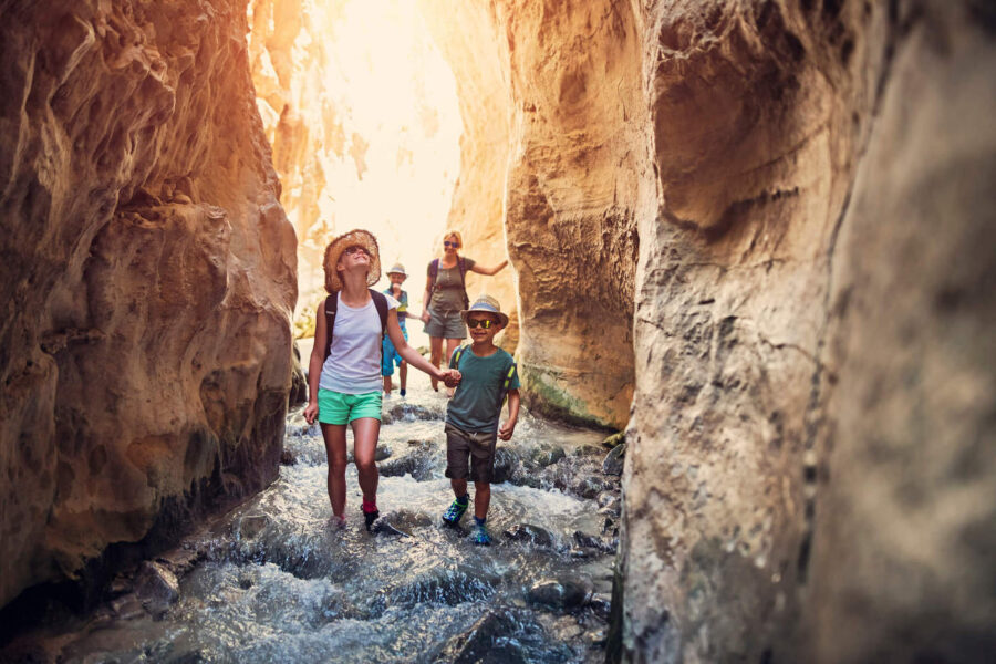 A family of four hikes inside of a canyon with water flowing on the ground.