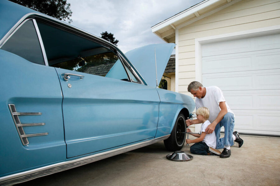 A father and son change a tire of a blue vintage car.