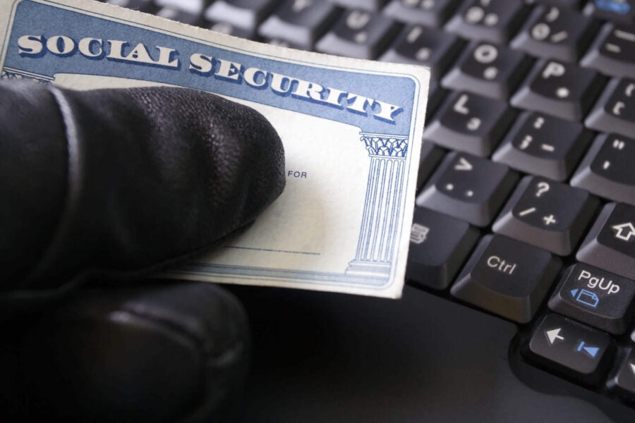 A hand wearing black gloves holds a social security card next to a black keyboard.
