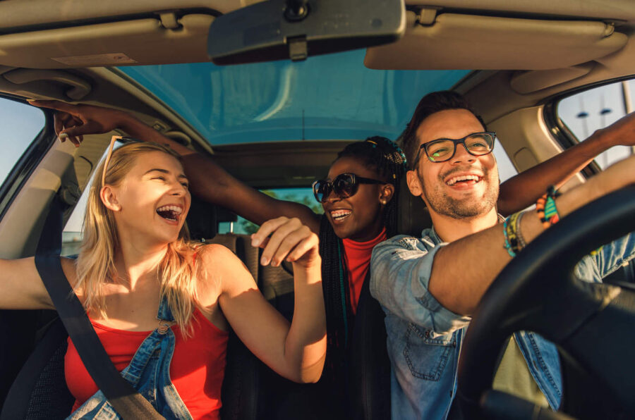 A group of three people smile and laugh together inside a car.