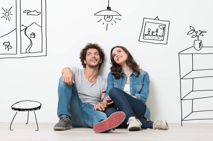 Happy Young Couple Sitting On Floor Looking Up While Dreaming Their New Home And Furnishing.