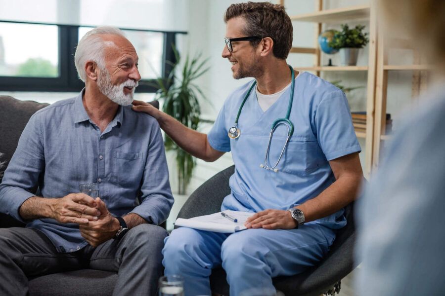 Happy doctor talking to senior male patient during a home visit.