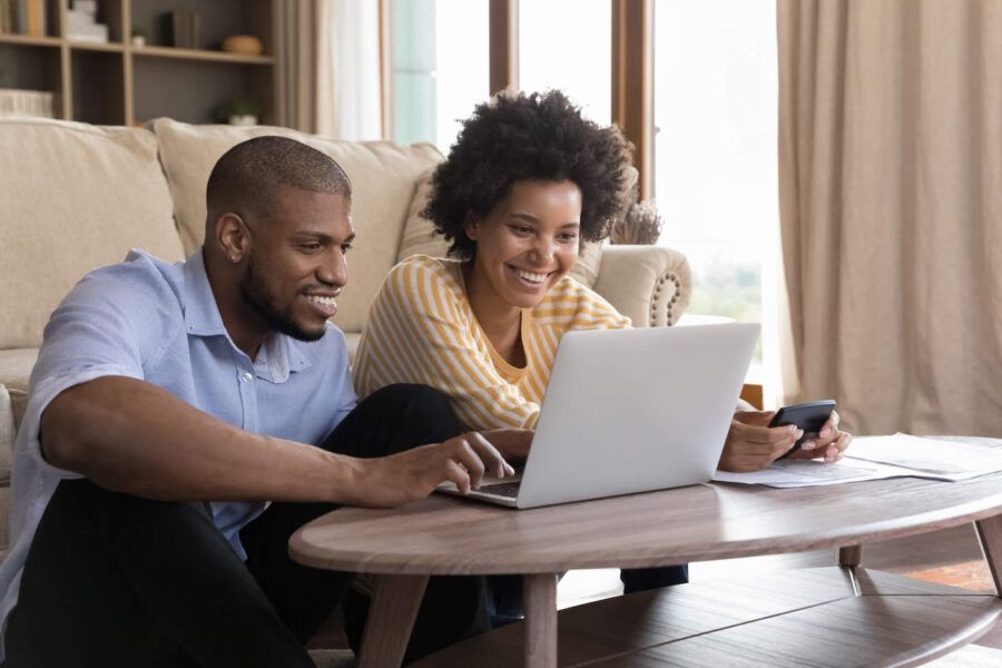 Happy young Black couple using laptop, looking at screen, smiling.