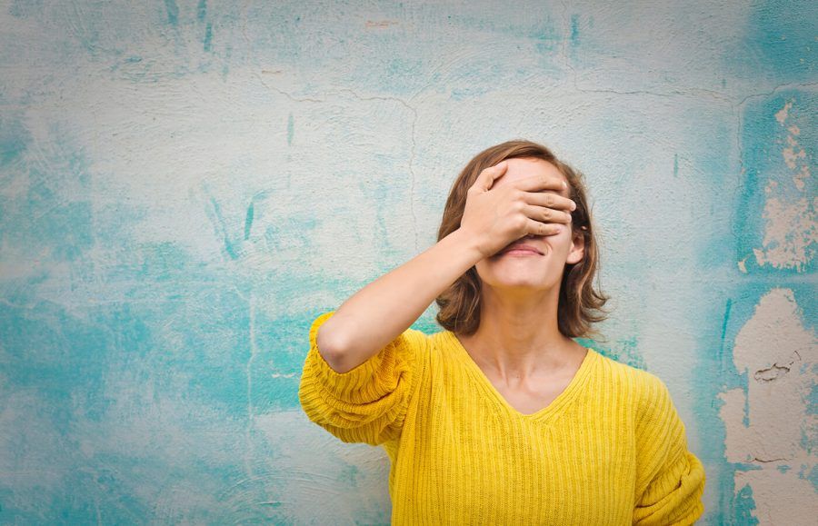 A woman facepalming in front of a blue wall.