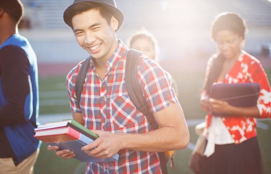 College students on the football field are carrying their text books with one college kid smiling.