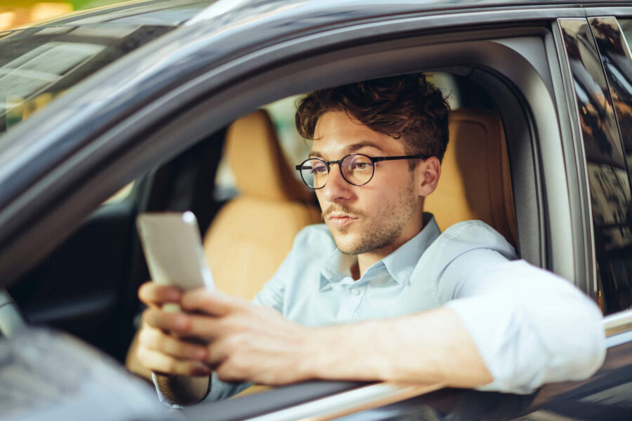 man seated in driver's side of car looking pensively at phone