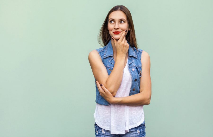 woman in denim vest thinking with a smile against a light green background