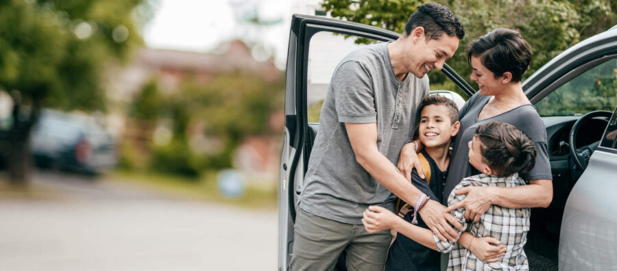family of four embracing beside a car