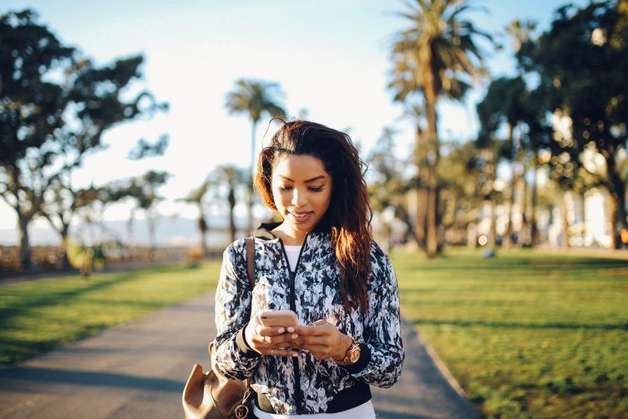 woman in jacket typing on phone against palm trees background