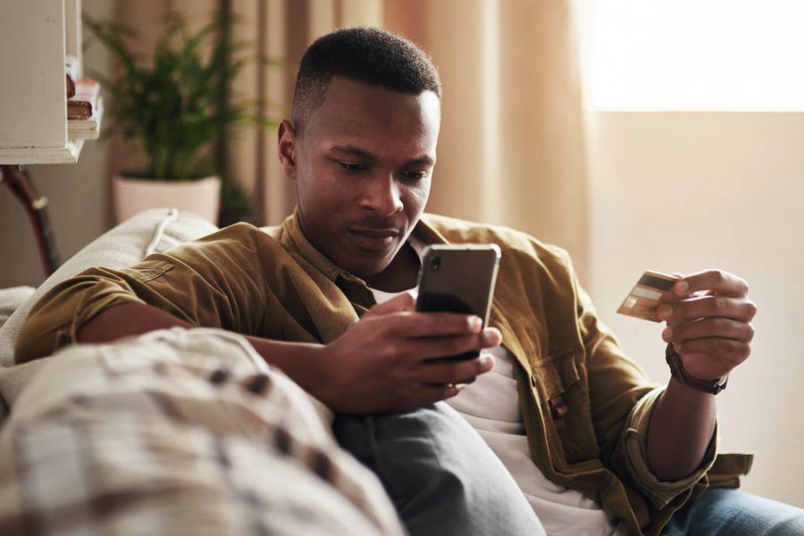 Cropped shot of a handsome young man using a smartphone and a credit card while sitting on his couch at home.