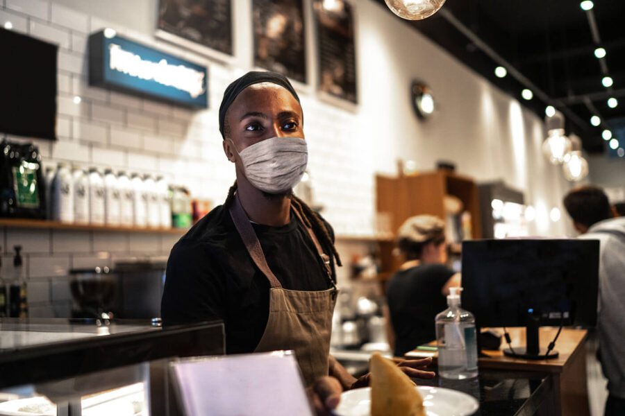 Young waiter with face mask working in coffee shop 