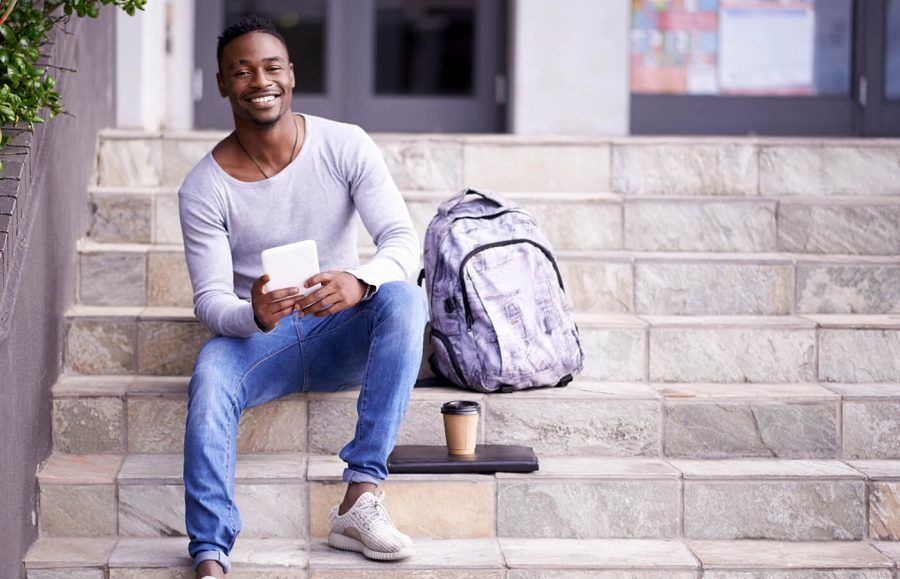 man in long sleeve shirt and denim sitting on a step next to a backpack smiling
