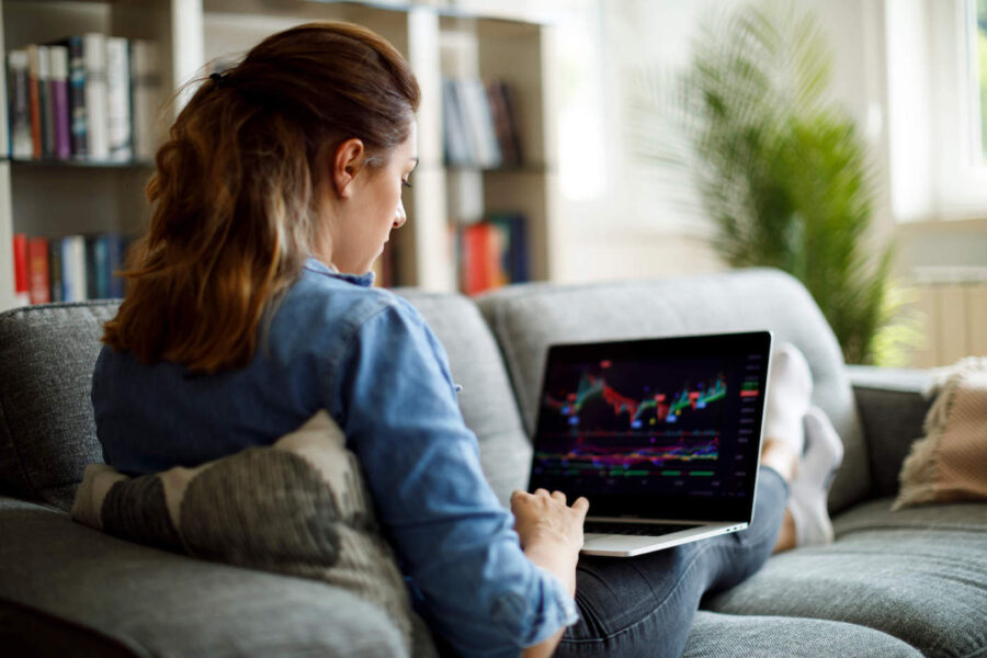 woman holding a laptop looking at investments while seated on a couch