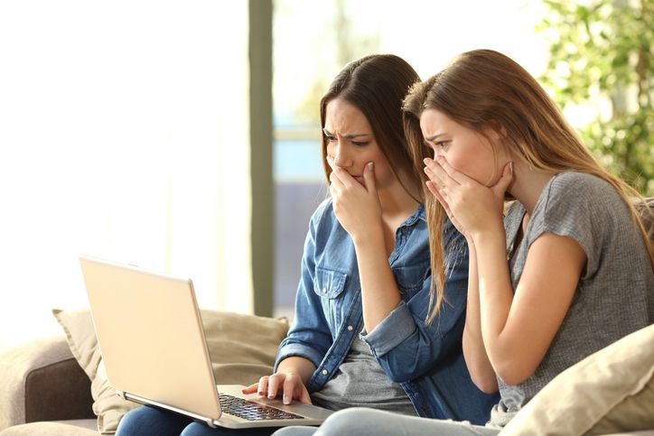 two young women cover their face in worry while looking at laptop screen