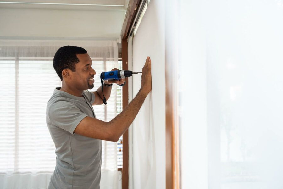 Smiling African American male using electric drill on the wall