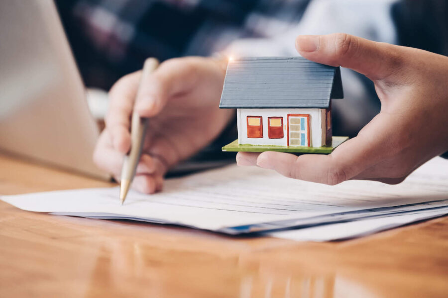 person signing mortgage paper holding a miniature house