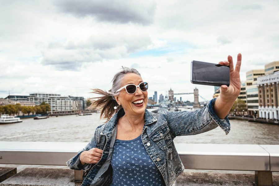 Senior tourist in London taking selfie with Tower Bridge in background -