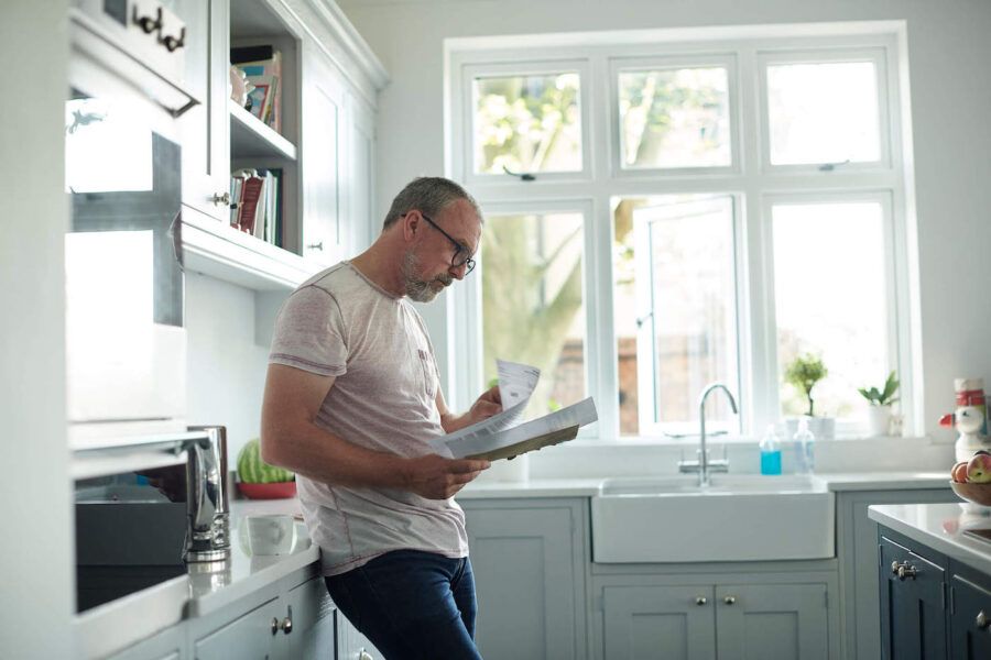 A man wearing glasses looks at documents in the kitchen.