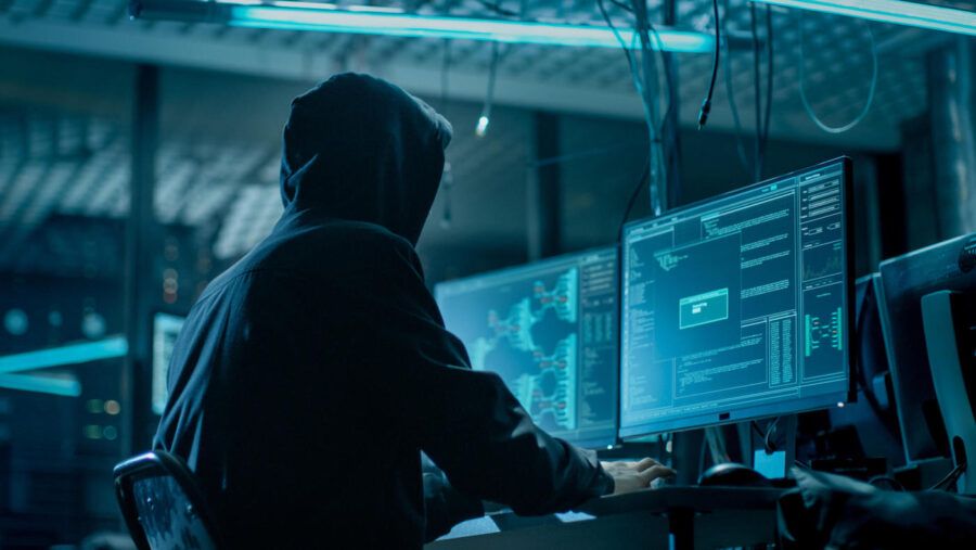 A man wearing a black jacket and hoodie uses a computer with wires hanging from the ceiling.