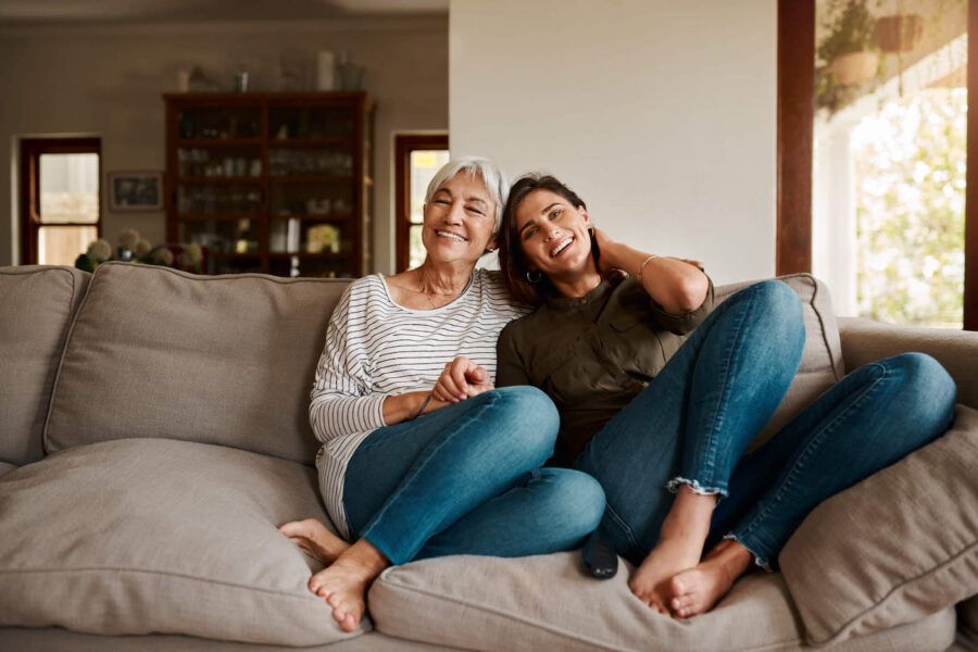 A mother and daughter smile together while sitting on the couch.