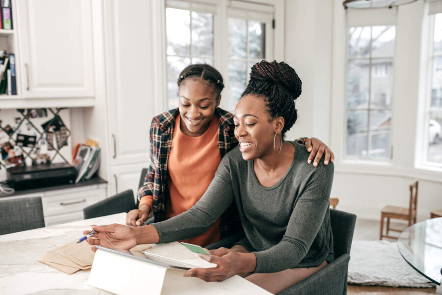 A mother and daughter are at their living room smiling at an iPad and the mother is holding a credit card.