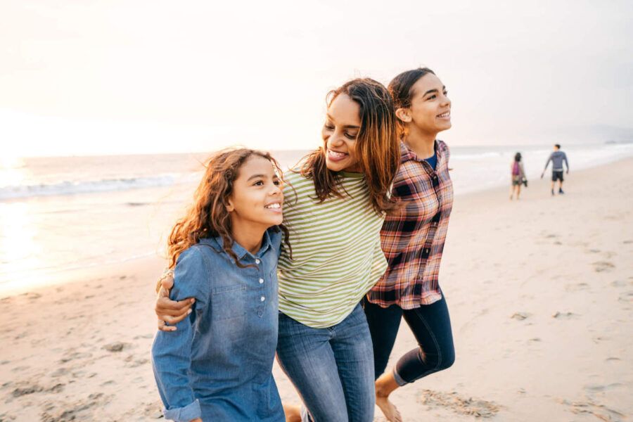 A mother smiles while at the beach with her daughters.