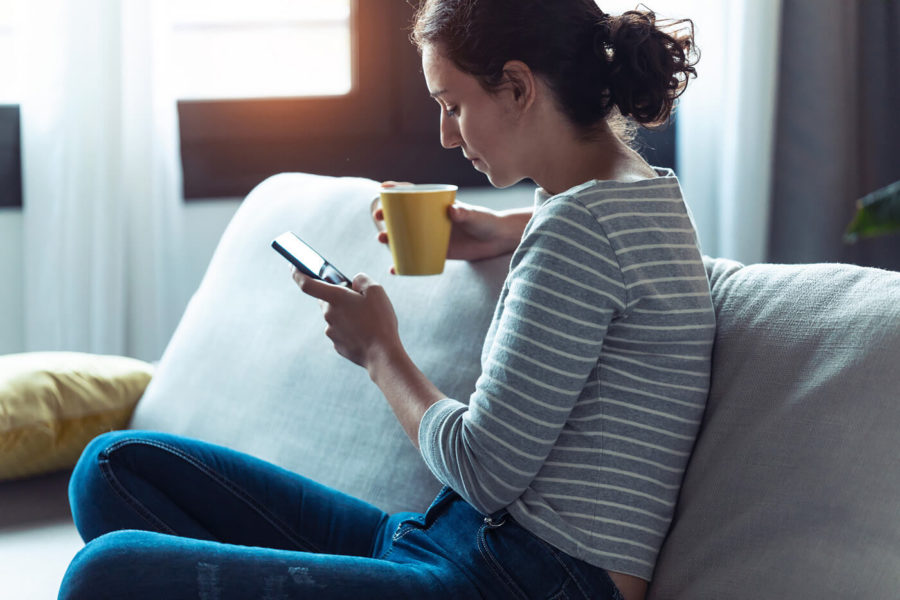 Serious young woman using her mobile phone while sitting on sofa in the living room at home