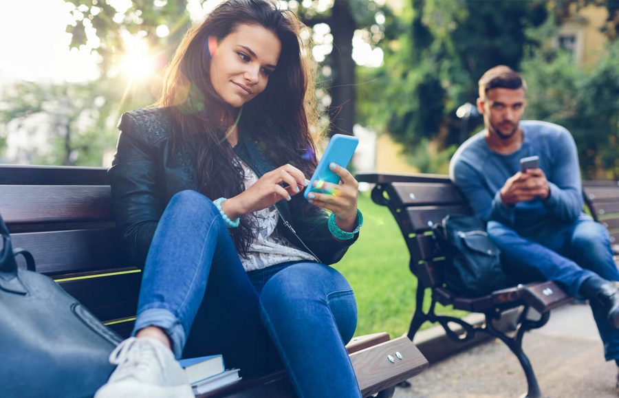 young woman sitting on a bench looking at phone planning retirement savings
