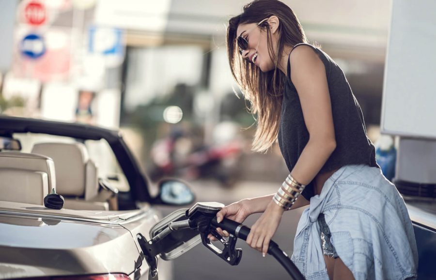 A woman smiling and putting gas in her convertible car with the top down.