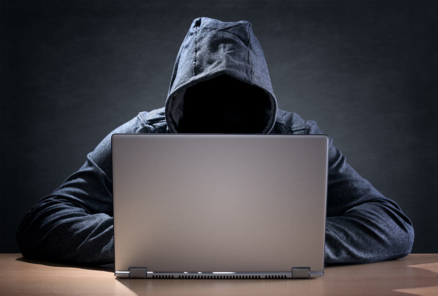 A person wearing a gray hoodie, with their face hidden, is typing on the computer next to gray background.