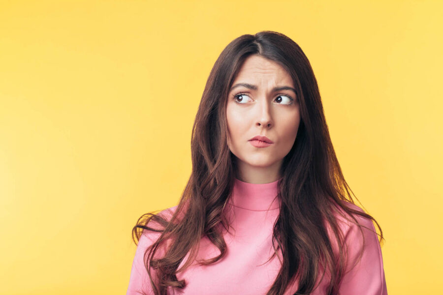 perplexed woman in pink sweater against yellow background