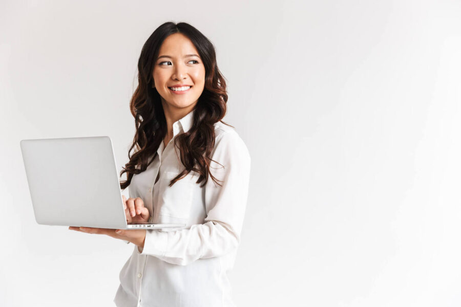 Smiling young asian businesswoman standing with laptop computer over white background, looking away.