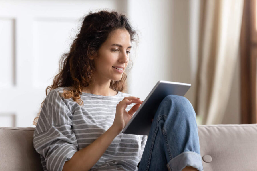 Smiling young woman using computer tablet, sitting on couch.