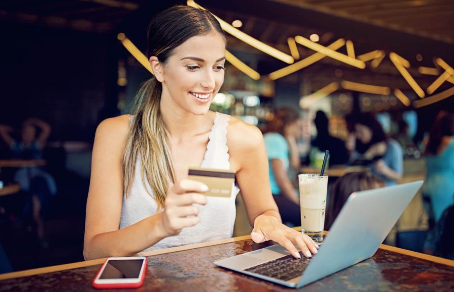 A woman sitting in a restaurant, using a laptop and holding a credit card.