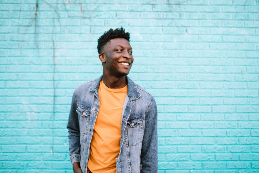 smiling man in denim jacket against blue brick wall