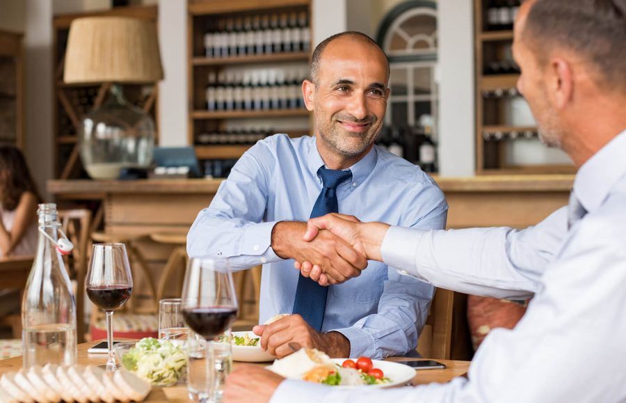 Two businessmen smiling and shaking hands at a business dinner.