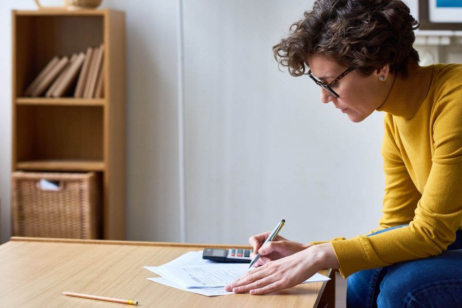 woman in yellow turtle neck and glasses leaning over coffee table writing with pen