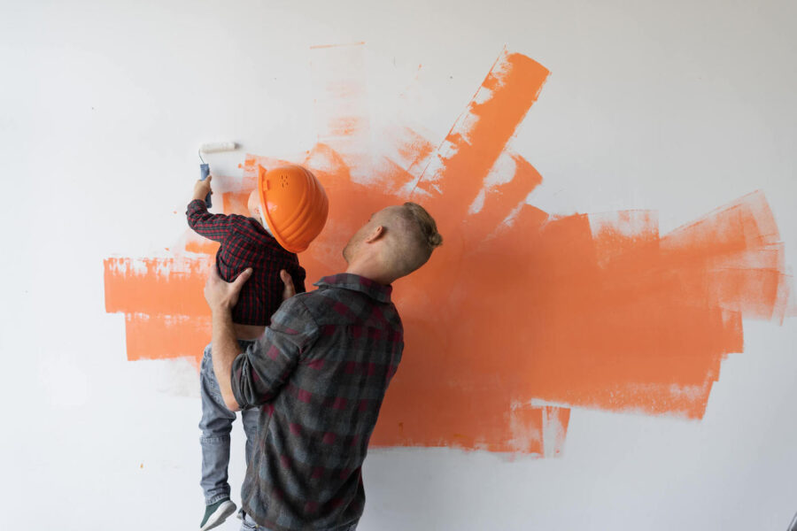 man holding young child while painting wall orange