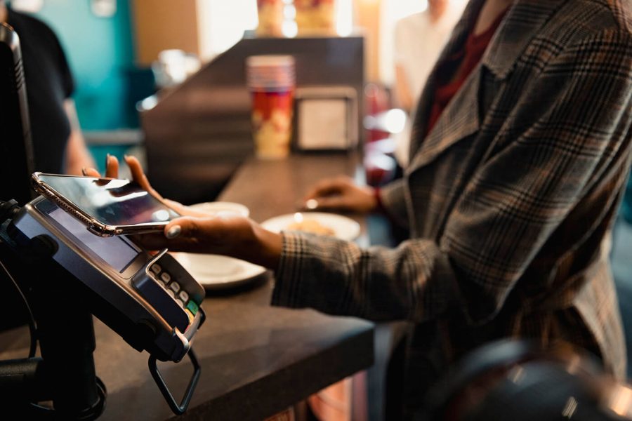 A person holds their phone to a card reader for contactless payment.