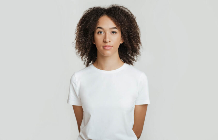 woman in white t-shirt holding folded hands in back against light grey backdrop