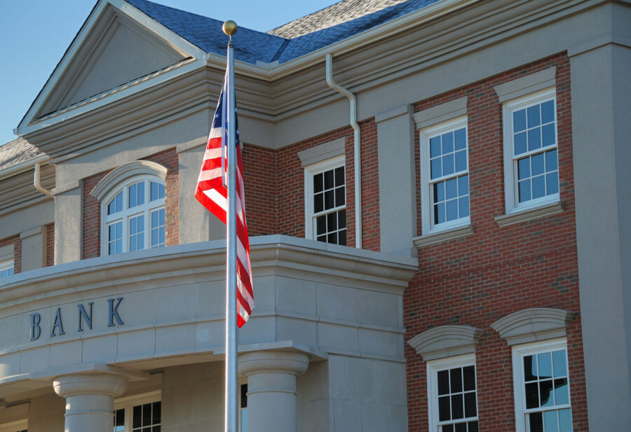 An American flag in front of a bank that is housed in a bricked building.