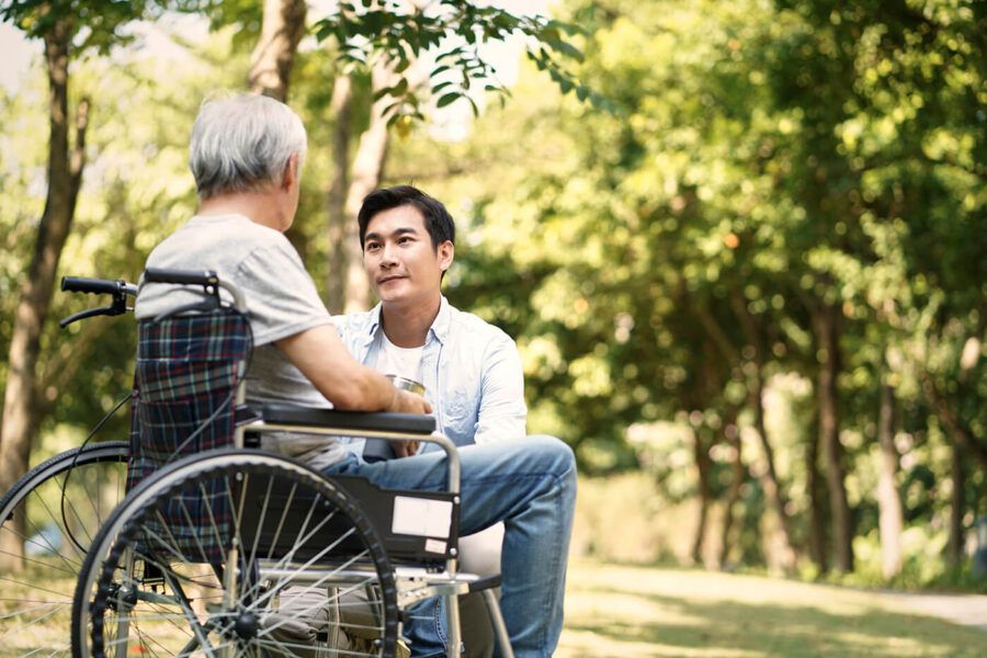 Asian son consoling wheelchair bound father outdoors