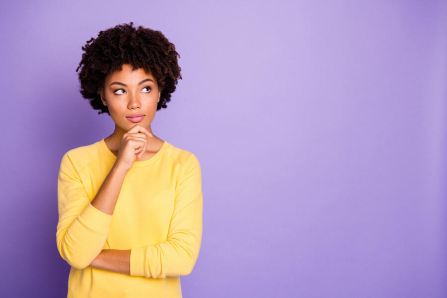 woman in yellow long-sleeve thinking against a purple background