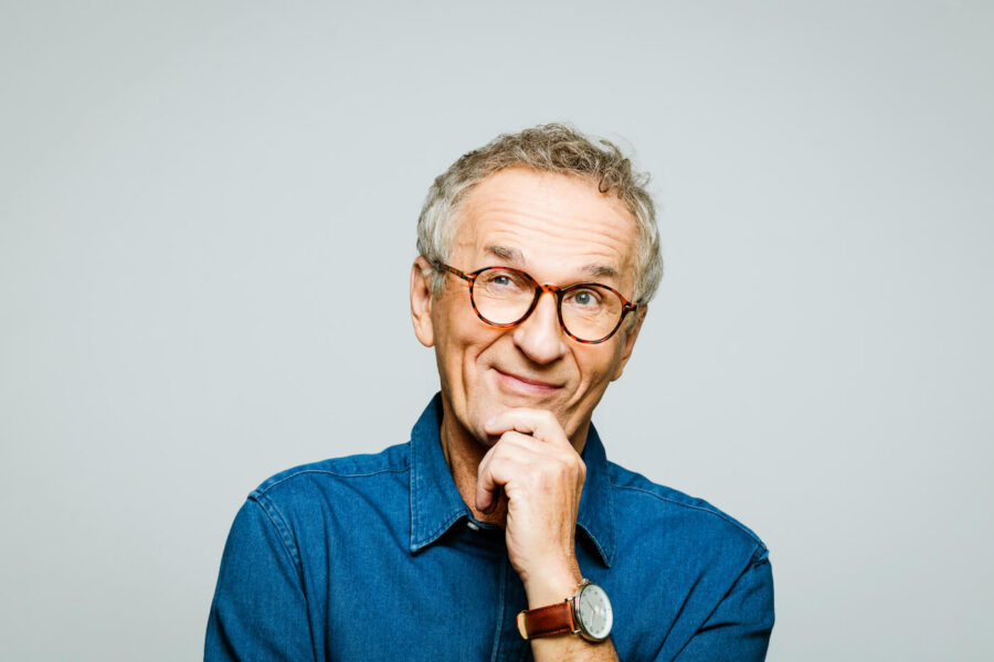 pensive older man with brown glasses against light grey background