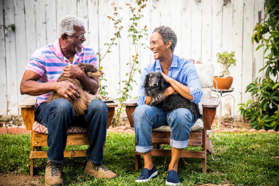 A senior couple sitting in chairs outdoors with their two dachshunds