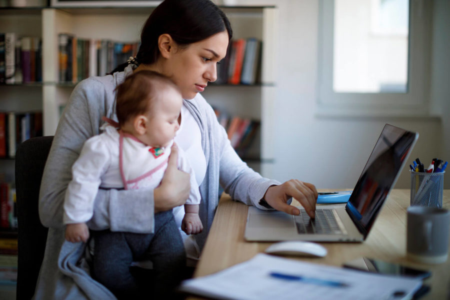 sitting woman holding baby and typing on a laptop