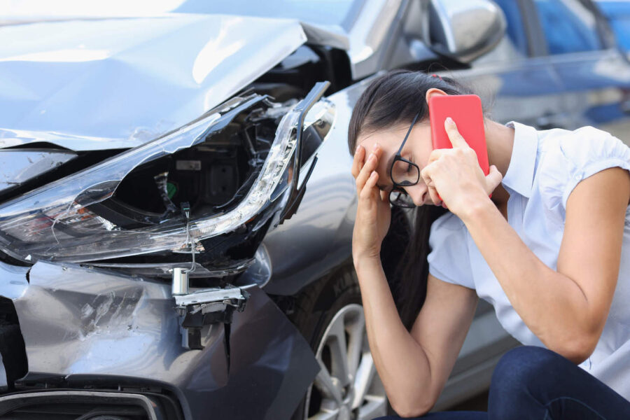 A woman has her hand to her head and talks on the phone while after a car accident that left her front car damaged.