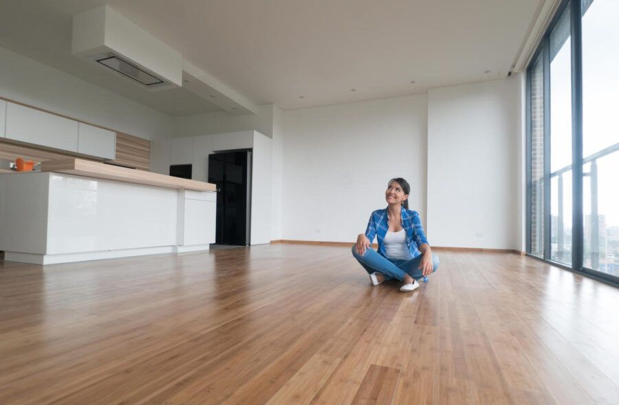 A woman smiles while sitting on the floor of an empty home.