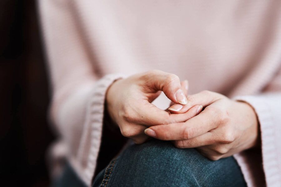 A woman wearing a pink sweater scratches her nails together while sitting down.